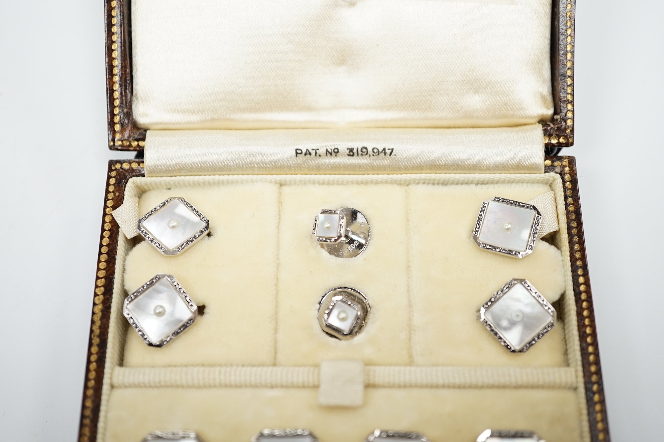 A 9ct white metal, mother of pearl and seed pearl set eight piece dress stud set, in fitted gilt tooled leather case.